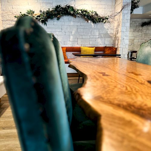 A modern dining space with a large wooden table, green chairs, and a brick wall adorned with greenery in the background.