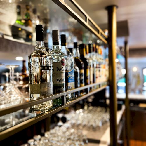 A bar shelf stocked with various liquor bottles and rows of glassware underneath, showcasing a neatly organized and inviting bar setup.