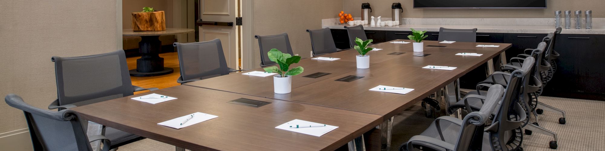 A modern conference room with a long table, chairs, a TV displaying 