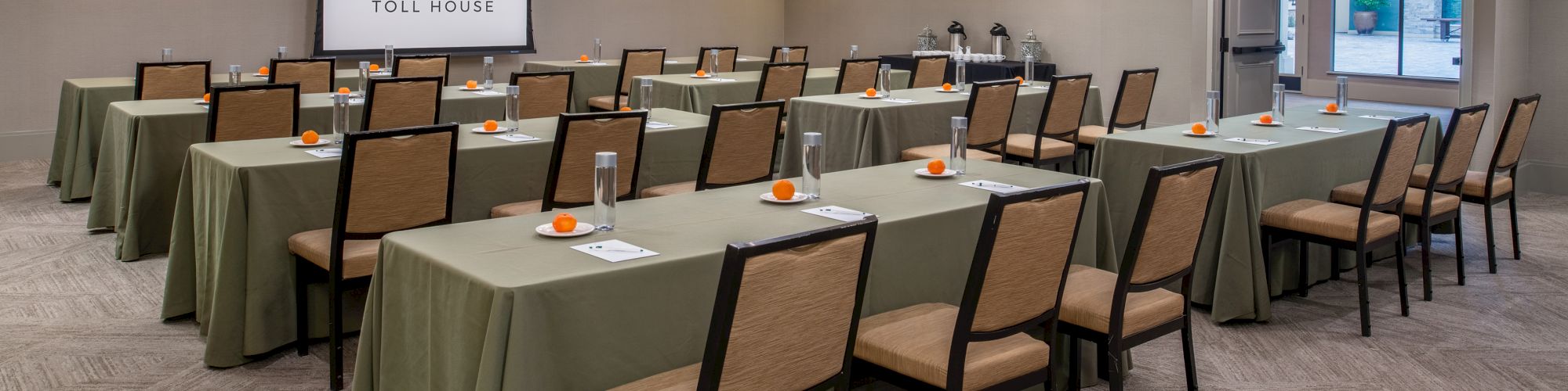 A conference room with multiple tables and chairs set up, a projection screen at the front, and decor on the tables, ready for a meeting.