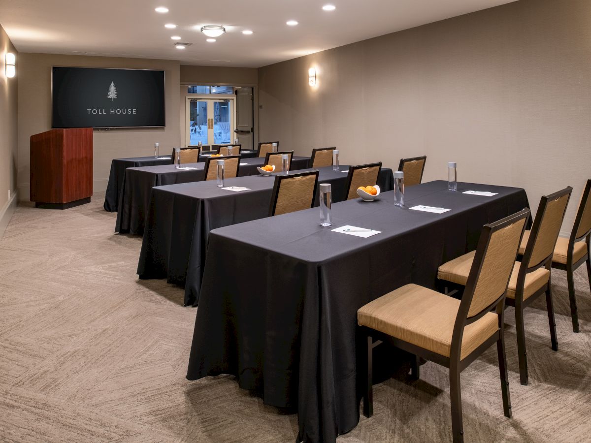 A small conference room with tables and chairs arranged in rows, a podium, and a screen at the front displaying 