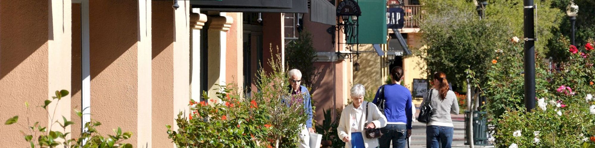 A charming street scene with shops, green awnings, vintage lamps, and people walking. The sign reads 