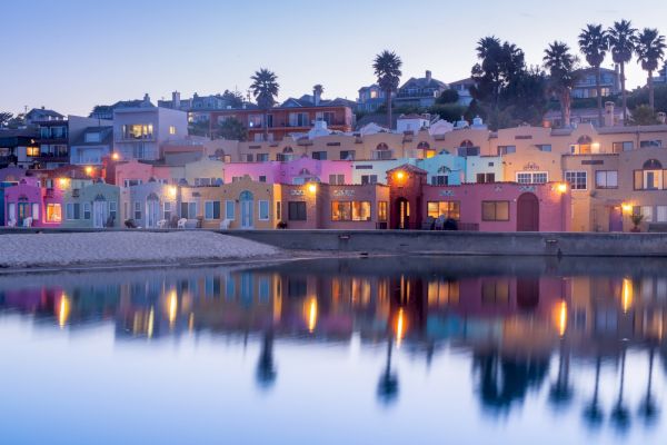 A serene waterfront scene with colorful buildings reflecting on calm water, with palm trees in the background and lights creating a tranquil ambiance.