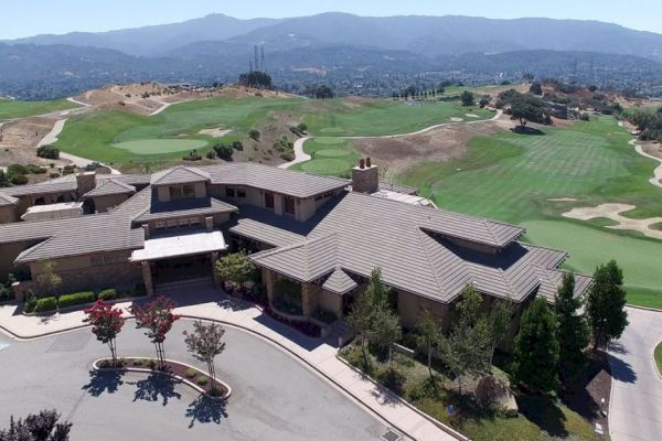 This image shows an aerial view of a large building complex surrounded by a sprawling golf course with mountains in the background.