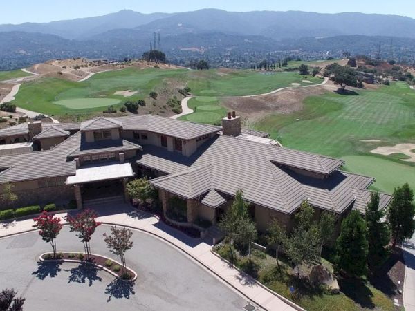 This image shows an aerial view of a large building complex surrounded by a sprawling golf course with mountains in the background.