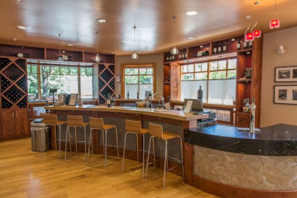 This image depicts a modern wine bar with wooden flooring, high chairs, a counter, and decorative wine racks, creating a cozy and inviting atmosphere.