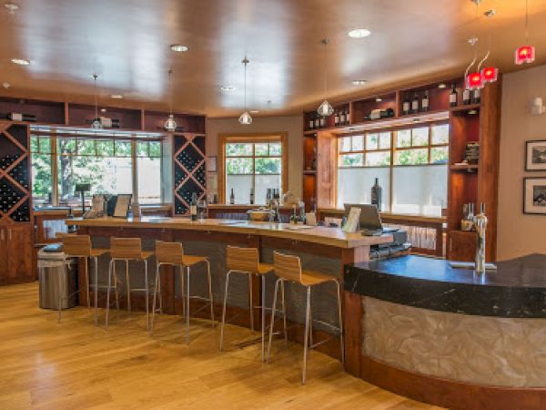 This image depicts a modern wine bar with wooden flooring, high chairs, a counter, and decorative wine racks, creating a cozy and inviting atmosphere.