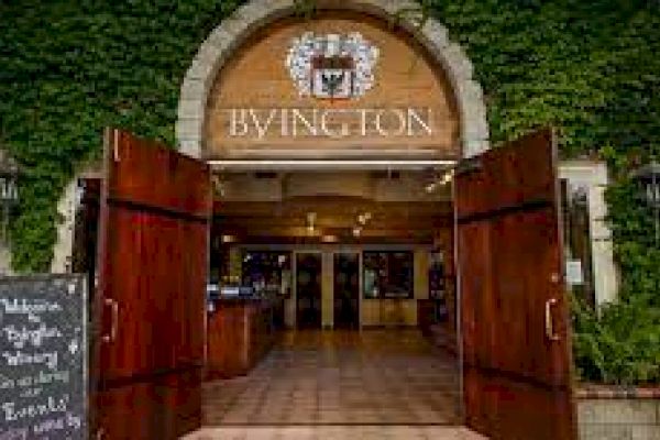 An entrance with wooden doors leads into a building with the sign "BYINGTON." Ivy covers the walls, and a chalkboard sign is by the door.