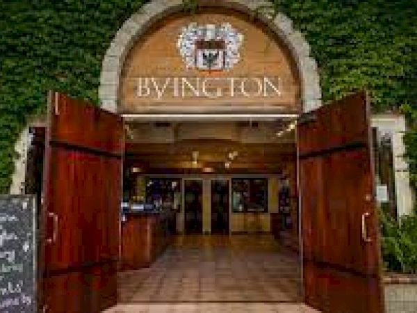 An entrance with wooden doors leads into a building with the sign "BYINGTON." Ivy covers the walls, and a chalkboard sign is by the door.