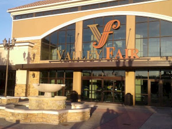 This image shows the entrance to "Valley Fair" with large glass windows, a sign above the entrance, and a circular fountain in the foreground.