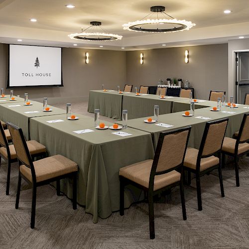 A conference room with U-shaped tables, notepads, and drinks setup. There is a projector screen displaying 