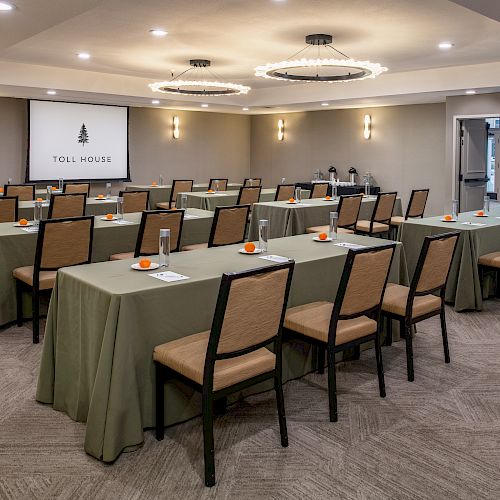 A conference room set up with rows of tables and chairs, a projector screen at the front, and orange accents on the tables.