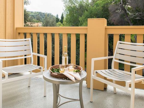 A cozy balcony with two white chairs and a small table holding a tray with a bottle, two glasses, and a refreshing drink garnish with greenery.