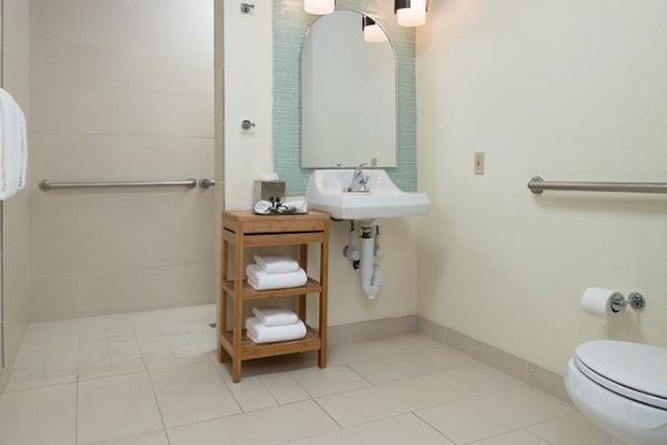 A bathroom with a walk-in shower, a sink with a mirror, and a storage unit with towels. The toilet has a grab bar nearby for accessibility.