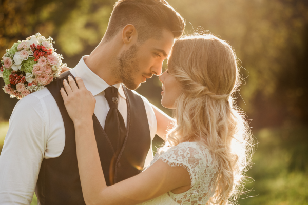 A couple is embracing outdoors, forehead to forehead, with the woman holding a bouquet of flowers in her right hand.