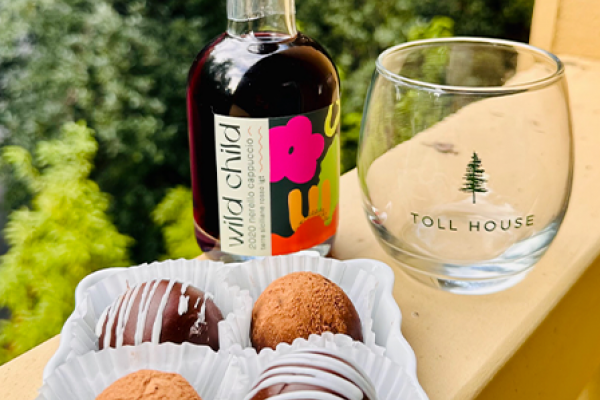 The image shows a bottle of "wild child" beverage, a Toll House glass, and a plate of four chocolate truffles with varied coatings, placed outside.
