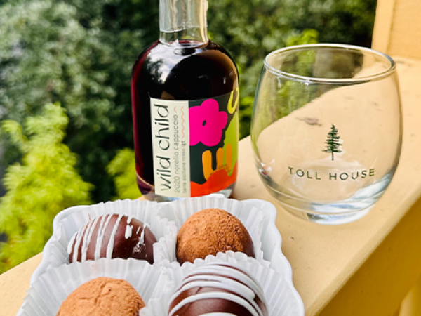 The image shows a bottle of "wild child" beverage, a Toll House glass, and a plate of four chocolate truffles with varied coatings, placed outside.