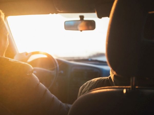 Two people are in a car, driving towards the setting sun.