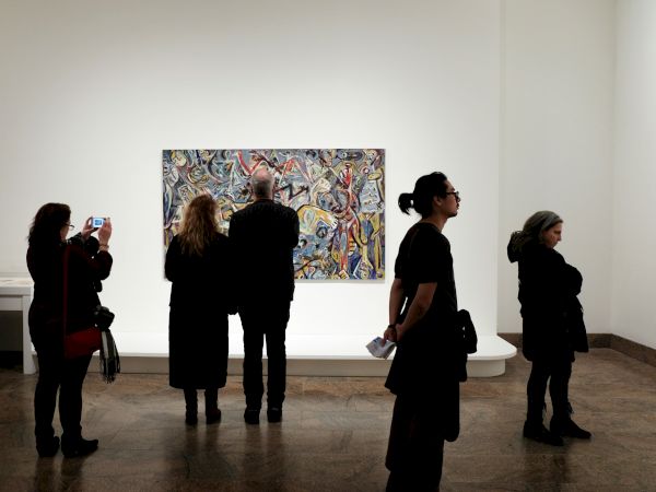 People viewing an abstract painting on a white wall in an art gallery.
