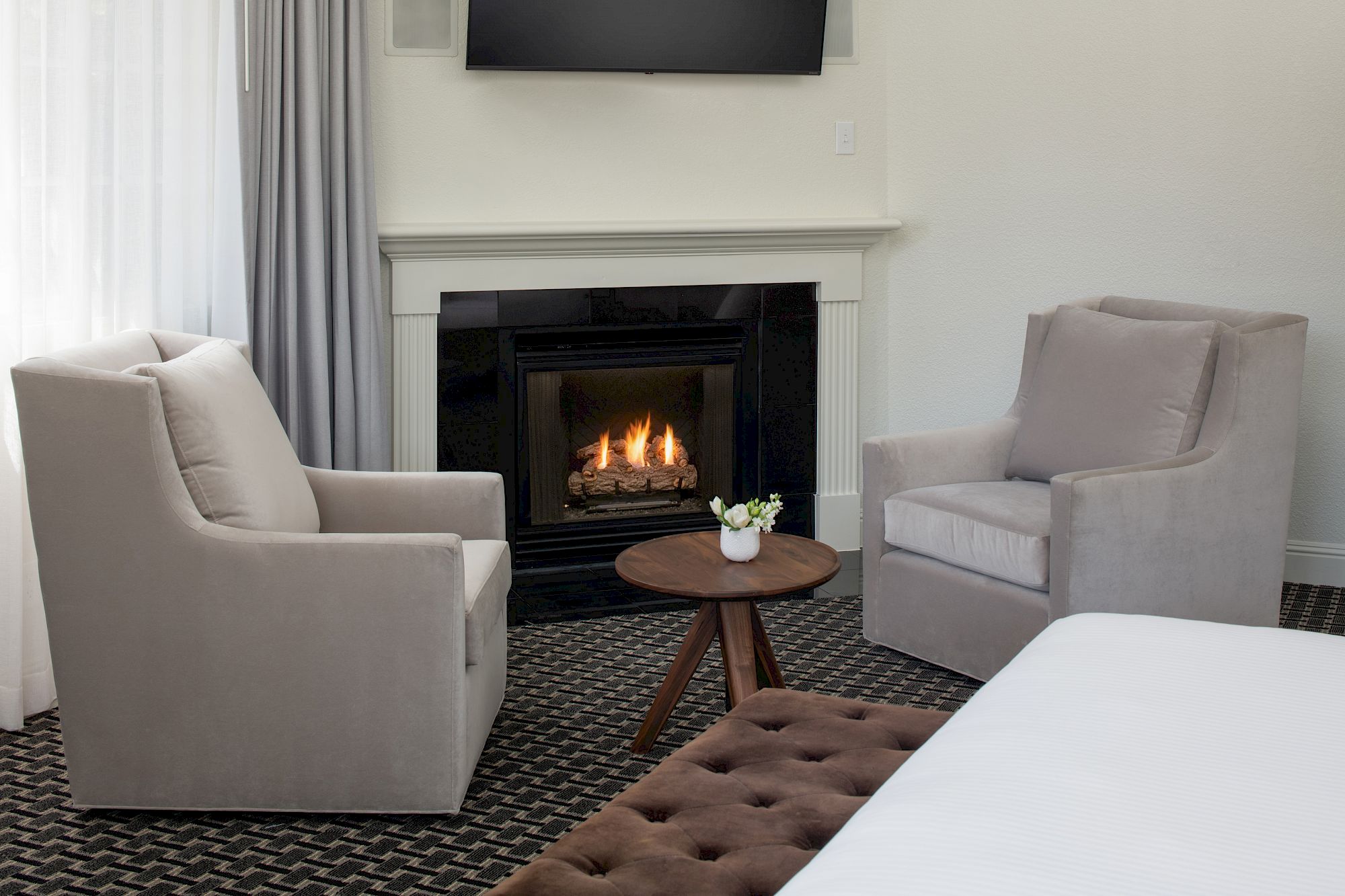 A cozy room with two armchairs, a small round table, a bed, and a lit fireplace, creating a warm and inviting atmosphere.