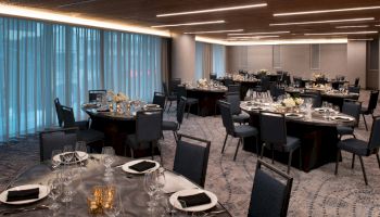 The image shows an elegantly set dining room with round tables, chairs, and floral centerpieces, ready for a formal event or reception.