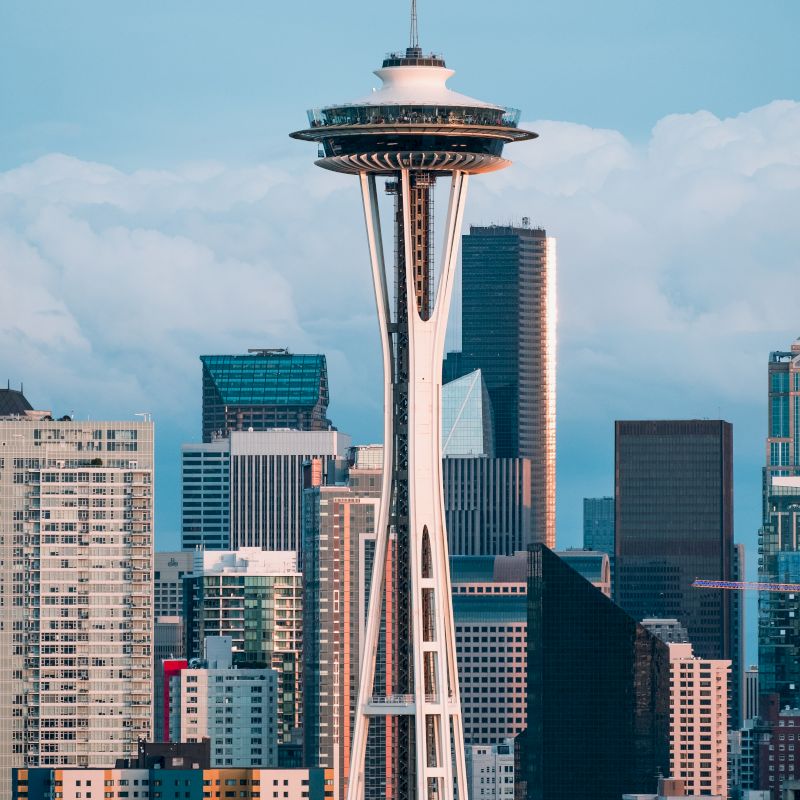 The image features the Space Needle, an iconic observation tower in Seattle, with a backdrop of modern buildings against a cloudy sky.