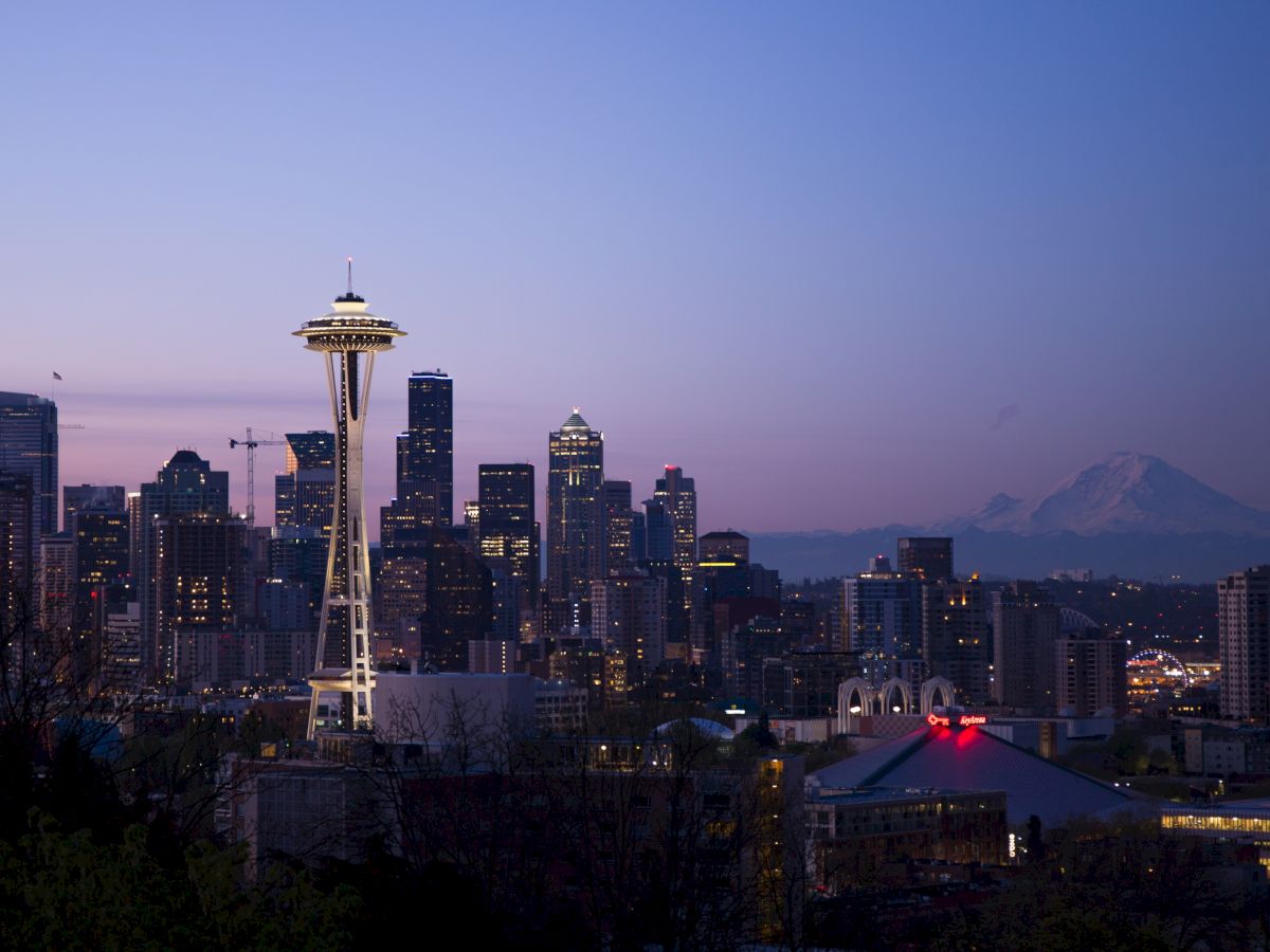 This image showcases the Seattle skyline at dusk, featuring the Space Needle and various skyscrapers, with Mount Rainier visible in the background.