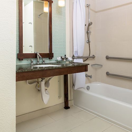 The image shows a bathroom with a sink, large mirror, white shower curtain, bathtub, and stainless steel grab bars on the shower walls.