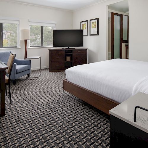 A modern hotel room with a bed, television, desk, chair, lamp, and two small vases with flowers on the bedside table and desk.