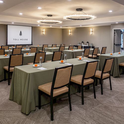 A conference room setup with tables and chairs, a projection screen at the front, and notepads and oranges placed on the tables.