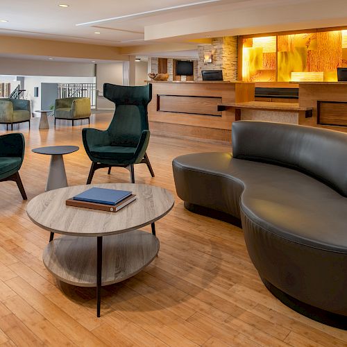 The image depicts a modern lobby with a curved black sofa, green armchairs, wooden tables, and a reception desk with an illuminated backdrop.